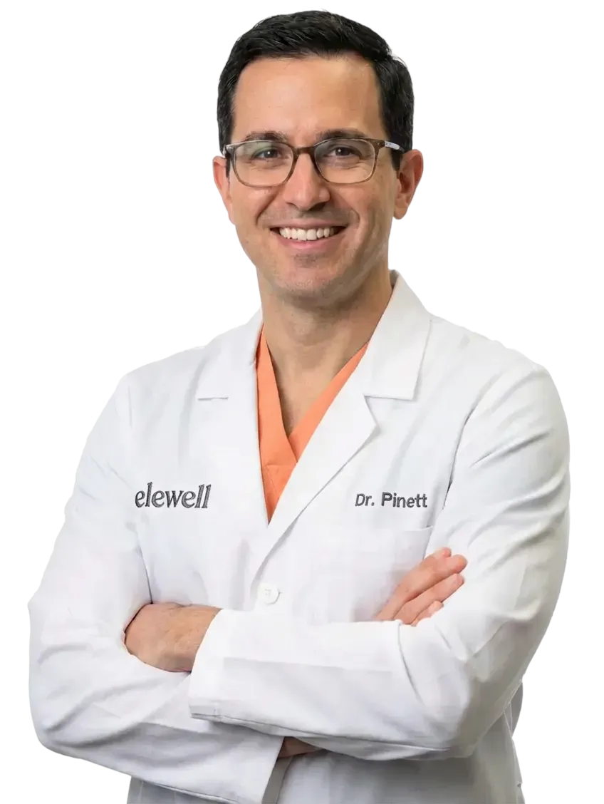 Portrait of Dr. Pinett, elewell medical provider, wearing a white lab coat and glasses.